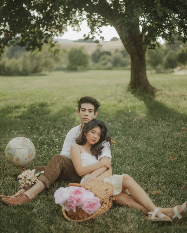 a man and woman sitting on the grass in front of a tree with a ball