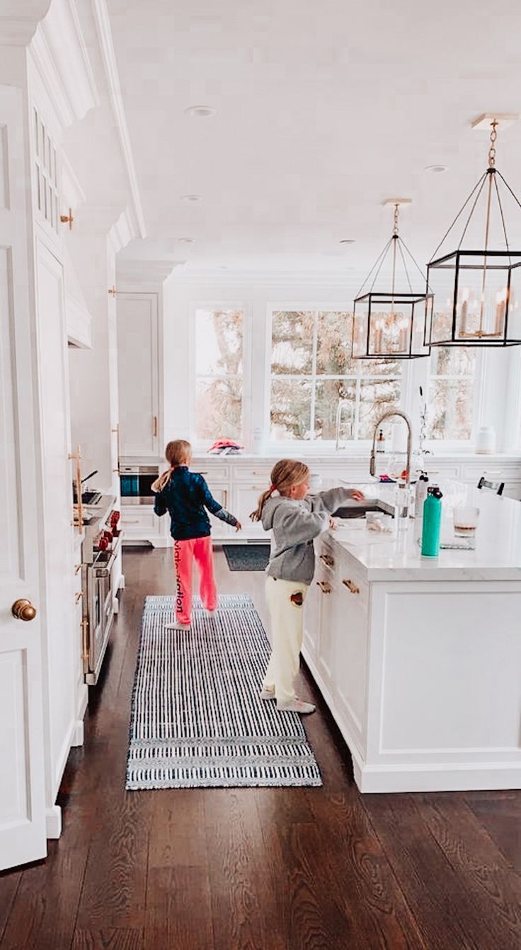 two young children are playing in the kitchen sink and on the floor, one is jumping up into the air