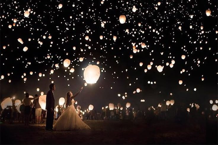 the bride and groom are surrounded by lanterns in the night sky at their wedding reception