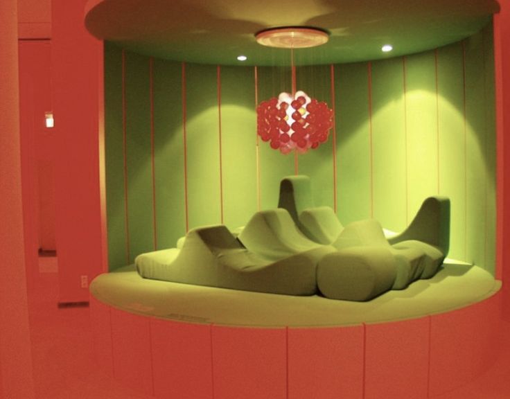 a room with green and red walls and furniture on the floor, in front of a circular light fixture