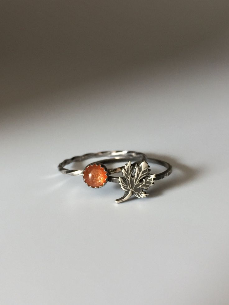 a silver ring with an orange stone on it and a leaf charm in the middle