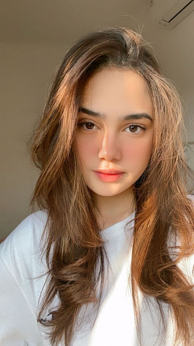 a woman with long brown hair wearing a white shirt and looking at the camera while she's taking a selfie