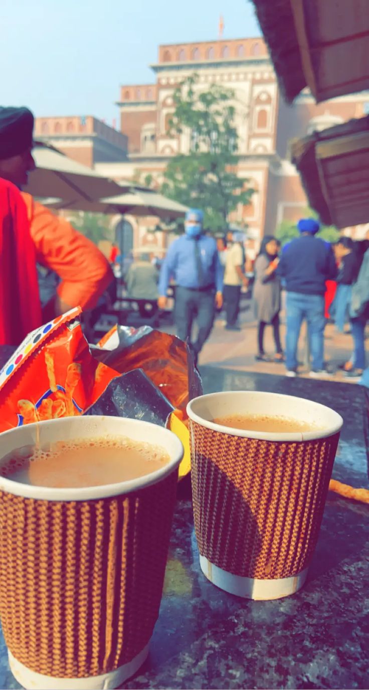 two cups of coffee sitting on top of a table next to people walking in the background