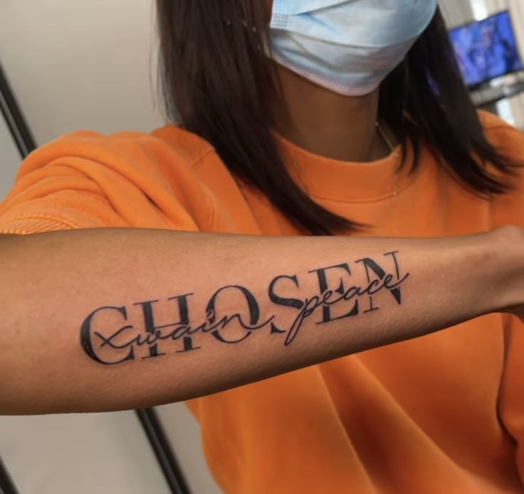 a woman wearing a face mask and holding her arm with the word chosen written on it