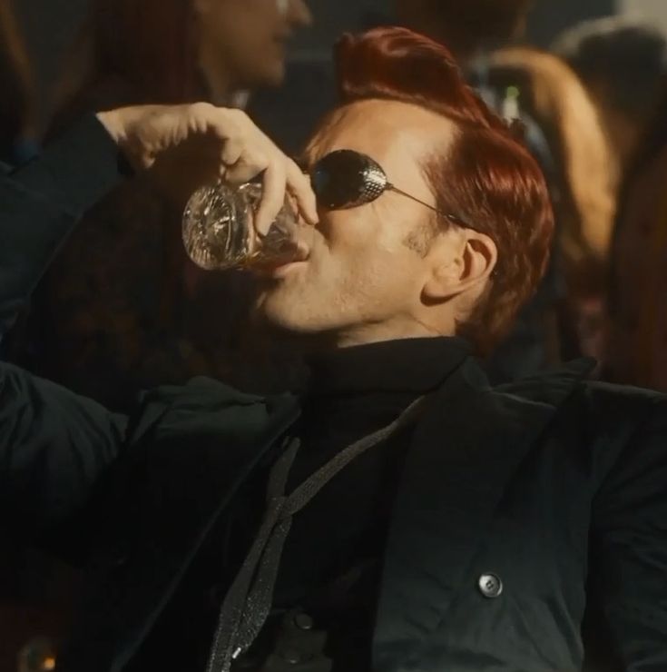 a man with red hair and sunglasses drinking from a glass in front of a crowd