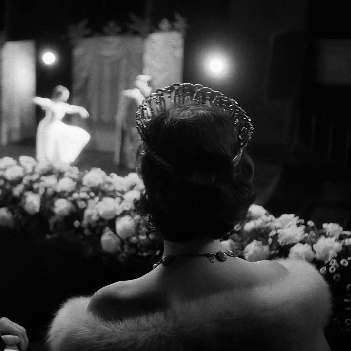 a woman wearing a tiara standing in front of a stage with flowers on it