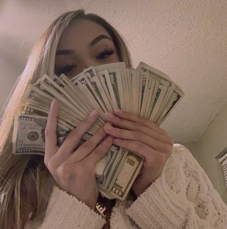 a woman covering her face with cash in front of her face and looking at the camera