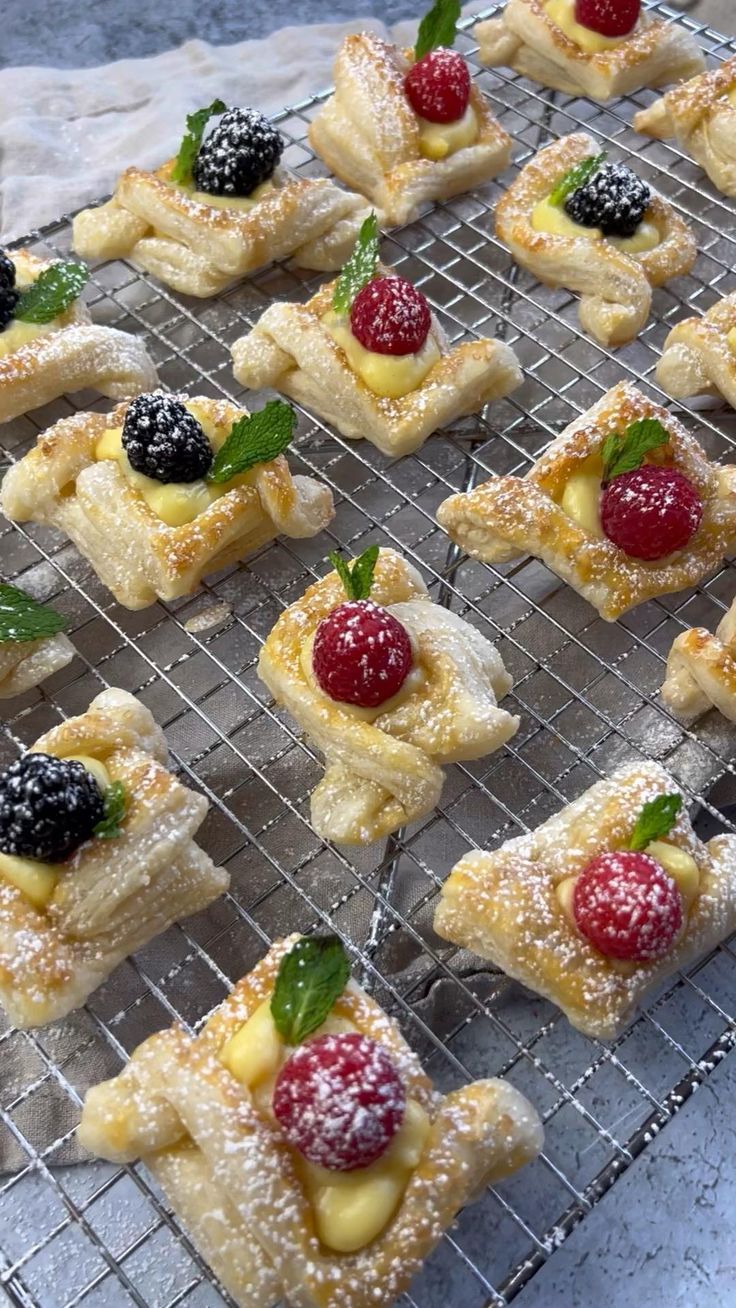 small pastries with berries and powdered sugar sit on a cooling rack, ready to be eaten