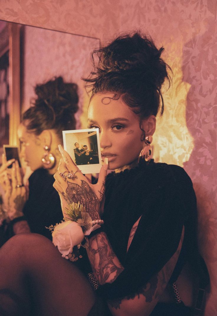 a woman sitting in front of a mirror with her hand up to her face and looking at the camera