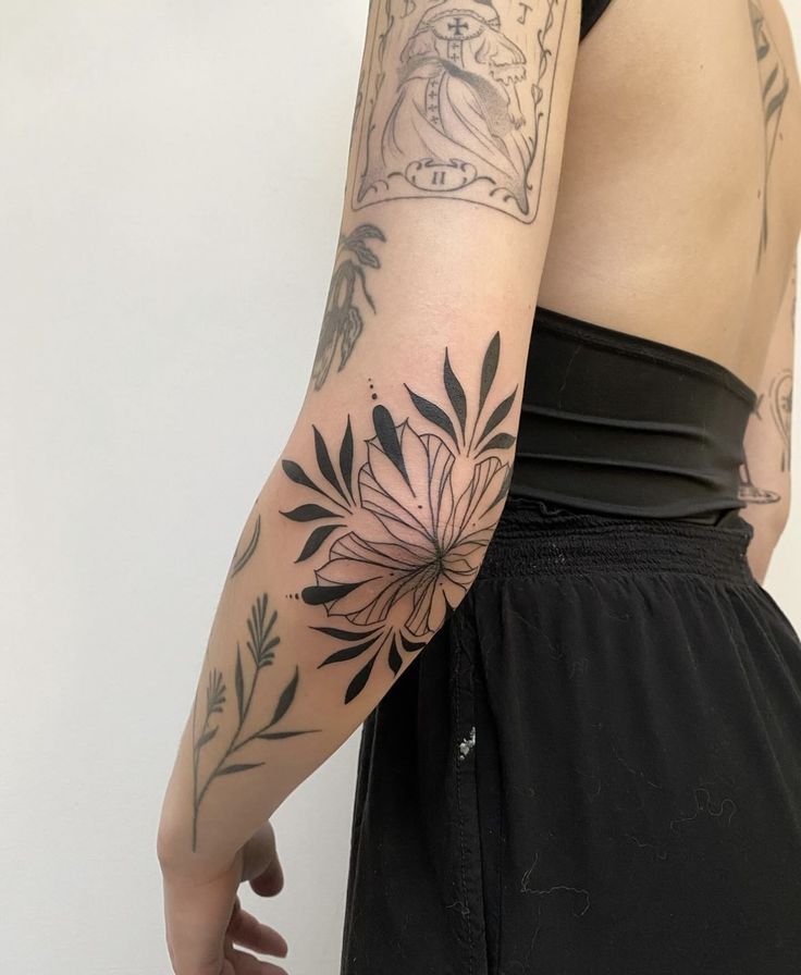 a woman's arm with tattoos on it and flowers in the middle, behind her