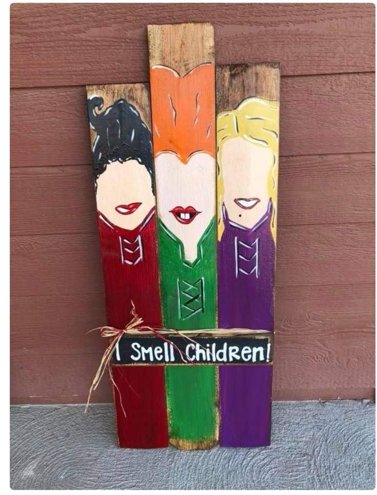 three painted wooden skis with the words i smell children written on one side and an image of two women's faces in different colors