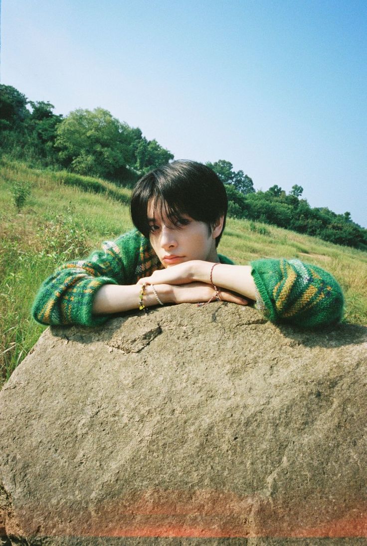 a young boy sitting on top of a large rock in the middle of a field