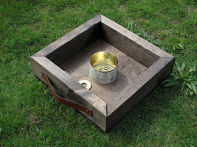 a wooden box sitting on top of a green grass covered field next to a metal cup