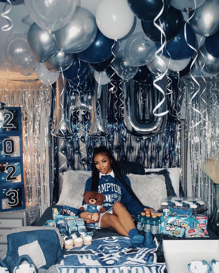 a woman sitting on top of a bed surrounded by blue and silver balloons, streamers and decorations