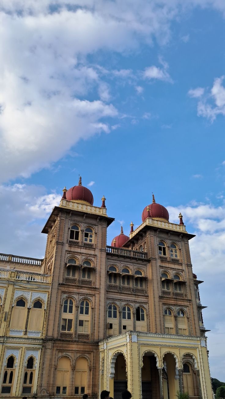 an old building with many windows and arches on the front, against a blue sky with white clouds