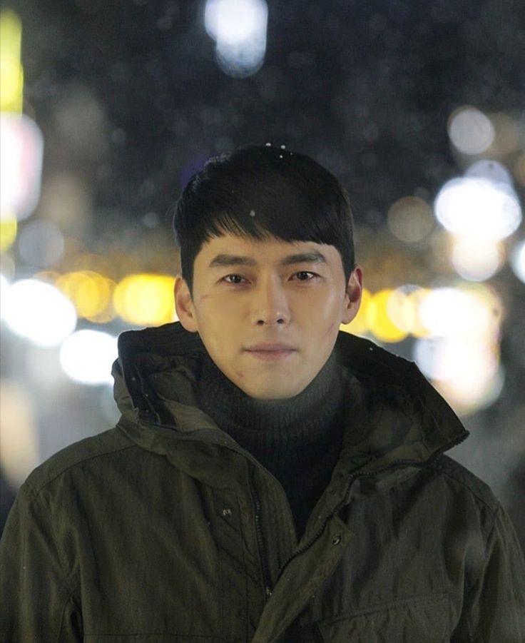 a young man standing in the middle of a street at night with lights behind him