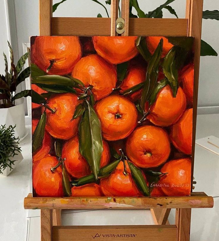 an easel with a painting of oranges on it's sides and leaves in the middle