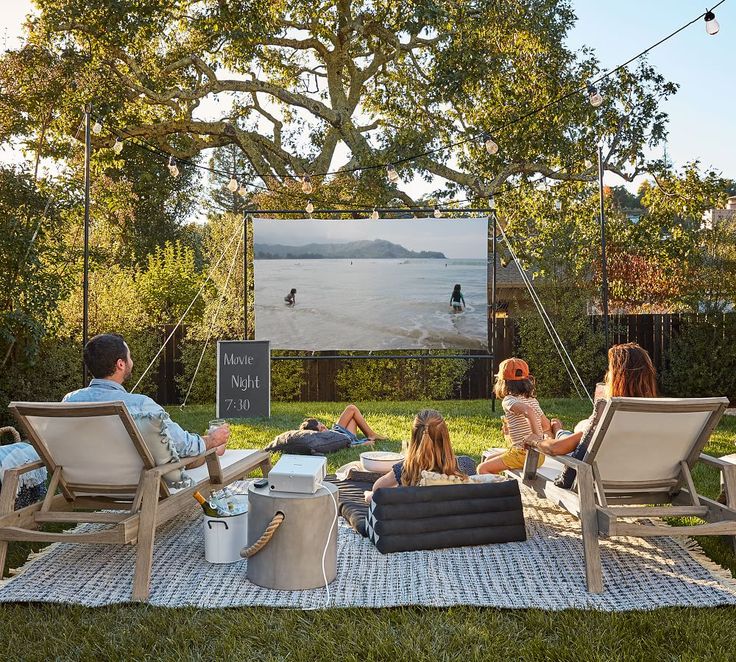 a group of people sitting on top of a blanket in front of a movie screen