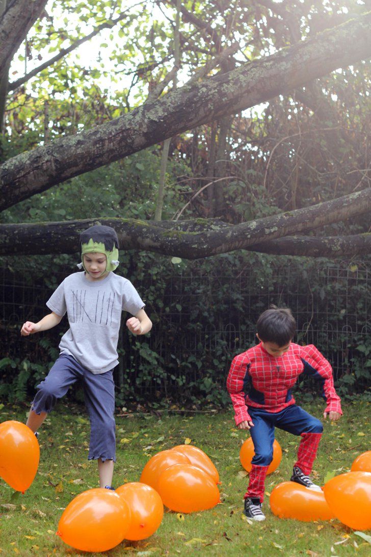 two young boys playing with orange balls in the grass, one boy wearing a spiderman costume