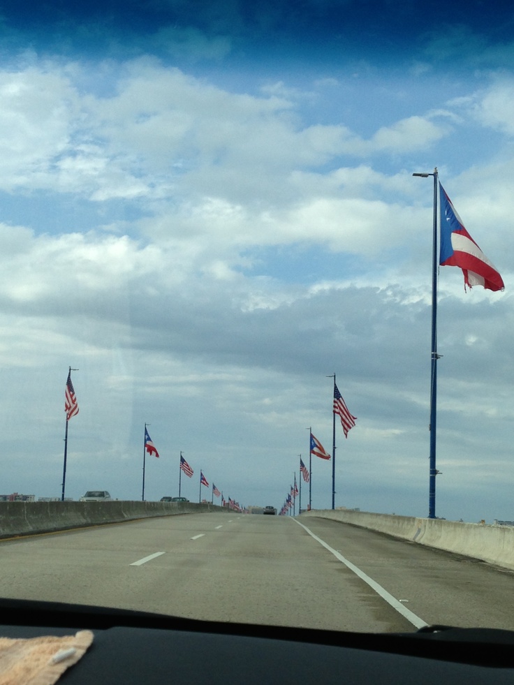 several american flags are flying in the wind on an empty highway with blue skies and white clouds