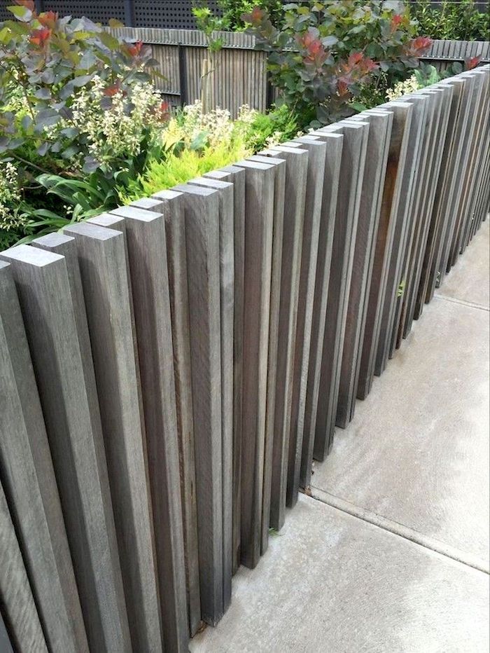 a wooden fence is lined with plants and flowers in the background, along with concrete walkways