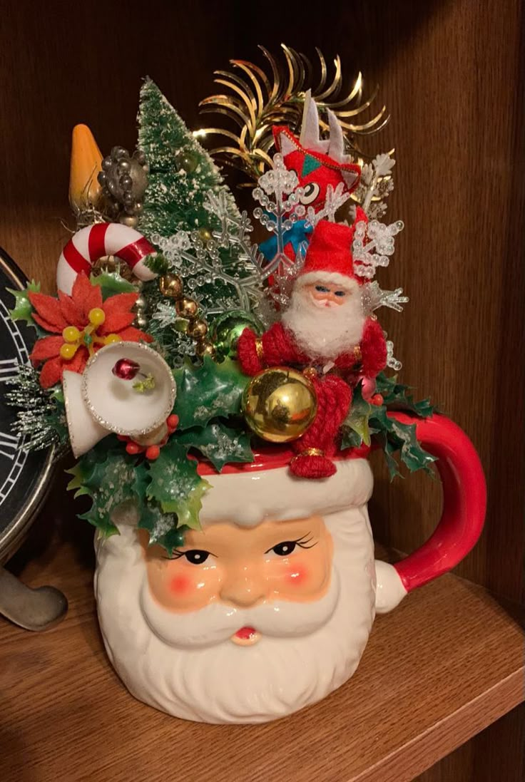 a santa claus mug with christmas decorations on it's head sitting on a shelf