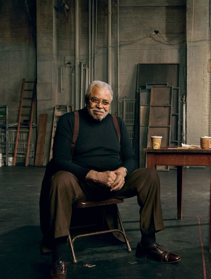 an older man sitting in a chair next to a wooden table with a cup on it