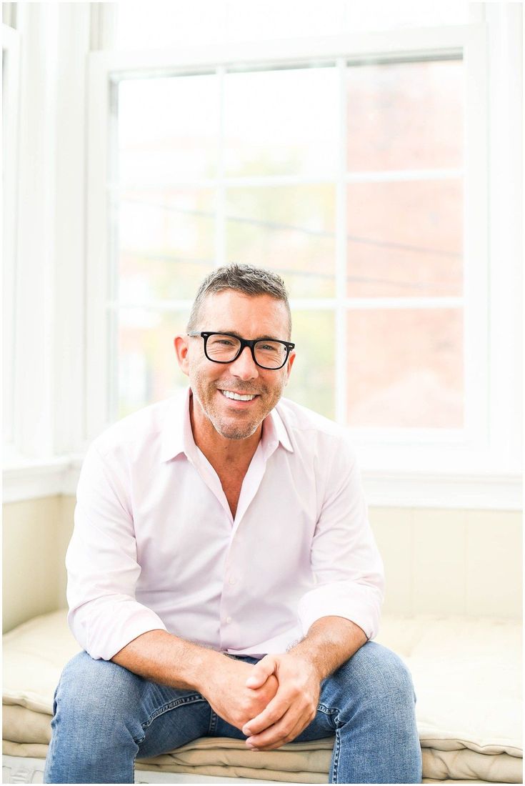 a man sitting on top of a couch in front of a window smiling at the camera