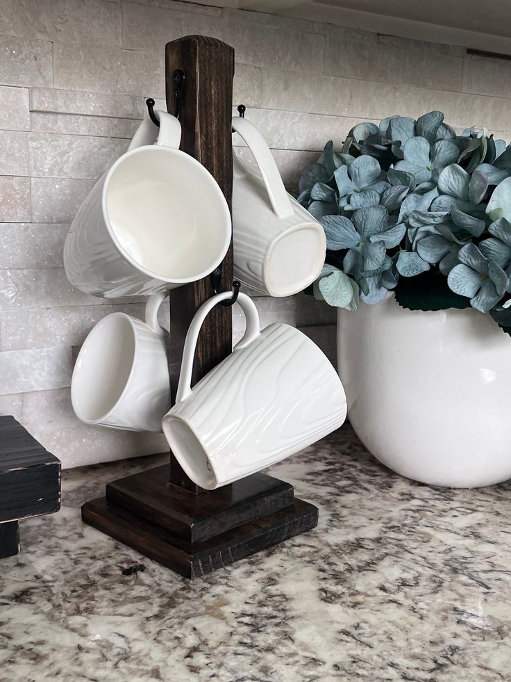 white cups and saucers are stacked on a wooden stand next to a potted plant