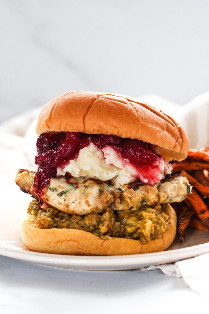 a chicken sandwich with cranberry sauce and sweet potato fries on a white plate