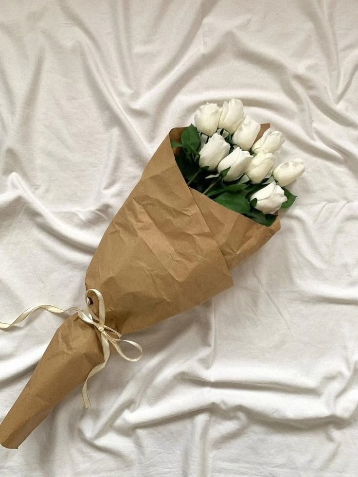 a bouquet of white tulips tied to a brown paper bag on a bed