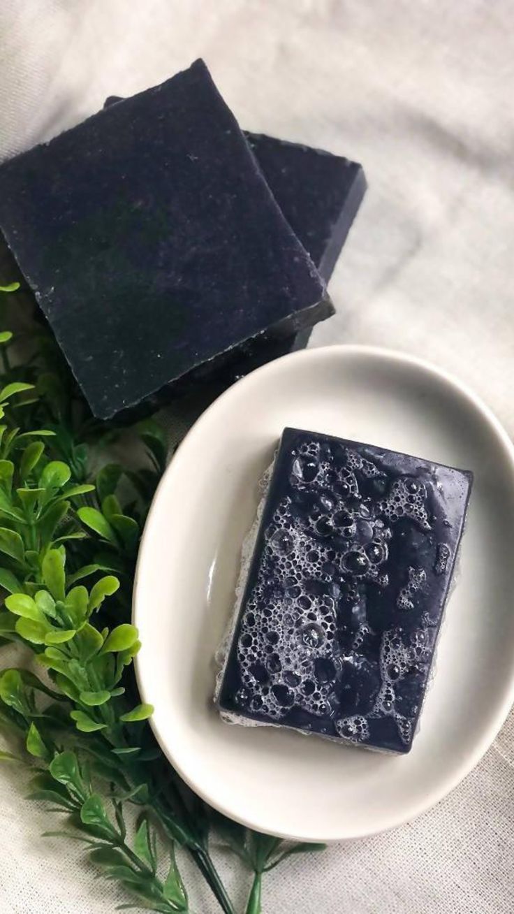 two soap bars sitting on top of a white plate next to some green plants and leaves