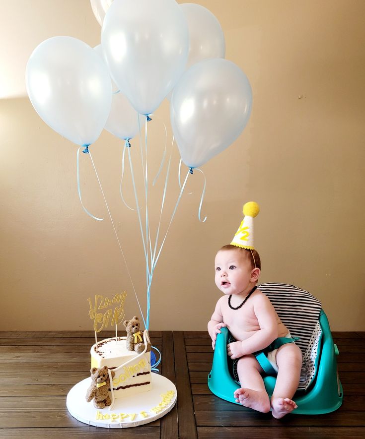 a baby sitting in front of a cake and balloons