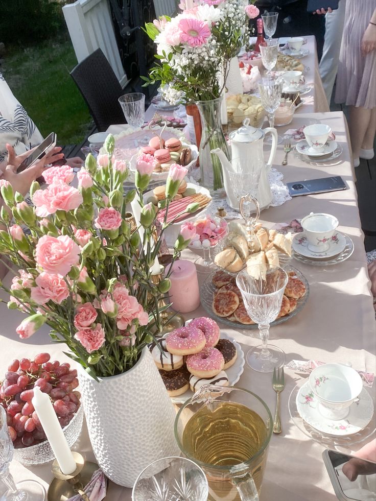 the table is set with pink flowers, plates and desserts for two people to eat