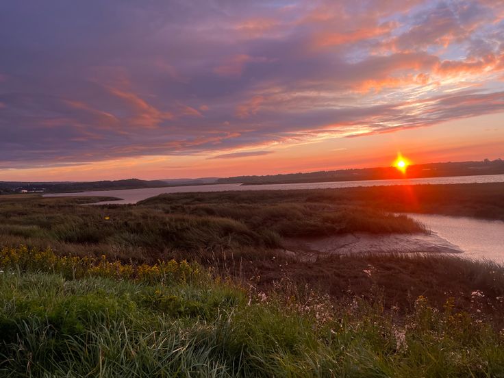 the sun is setting over some water and grass