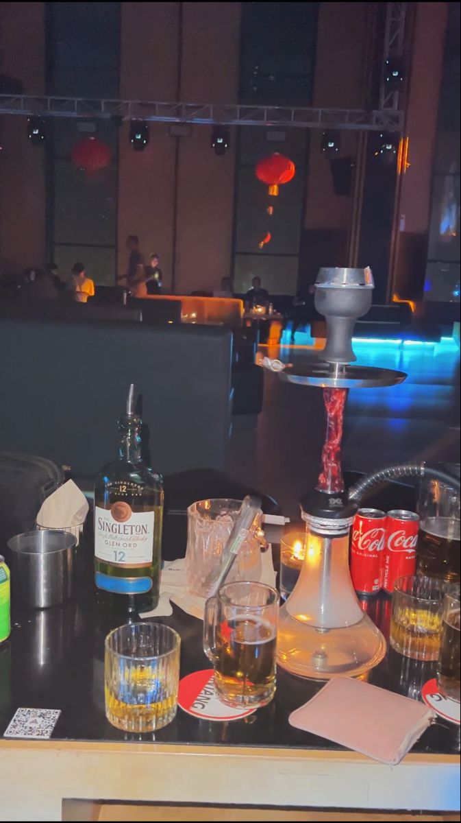 bottles and glasses sit on a table in a dimly lit room with other items around it