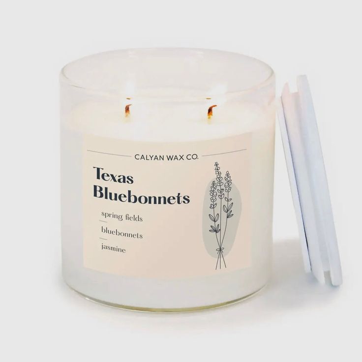 a candle that is sitting next to some white straws on a table with the words texas bluebonnets written in it