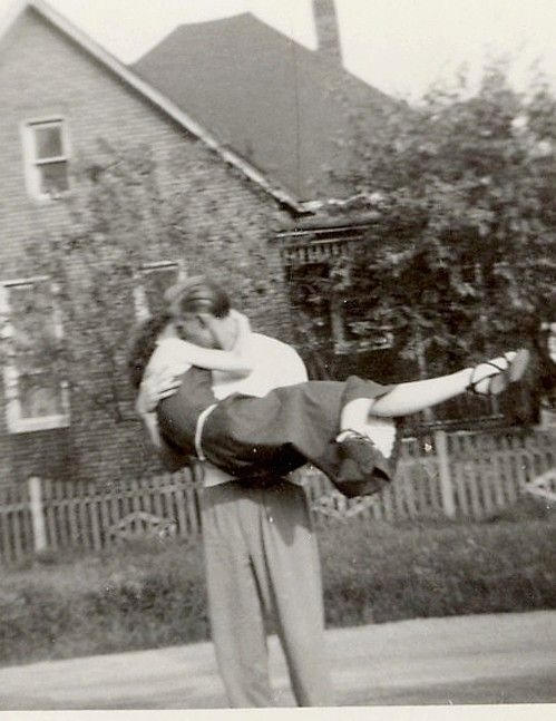 an old black and white photo of a man holding a woman on his back in front of a house