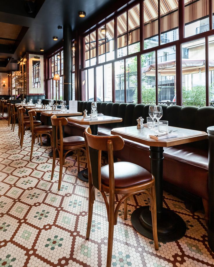 an empty restaurant with wooden tables and brown leather booths, windows, and patterned flooring