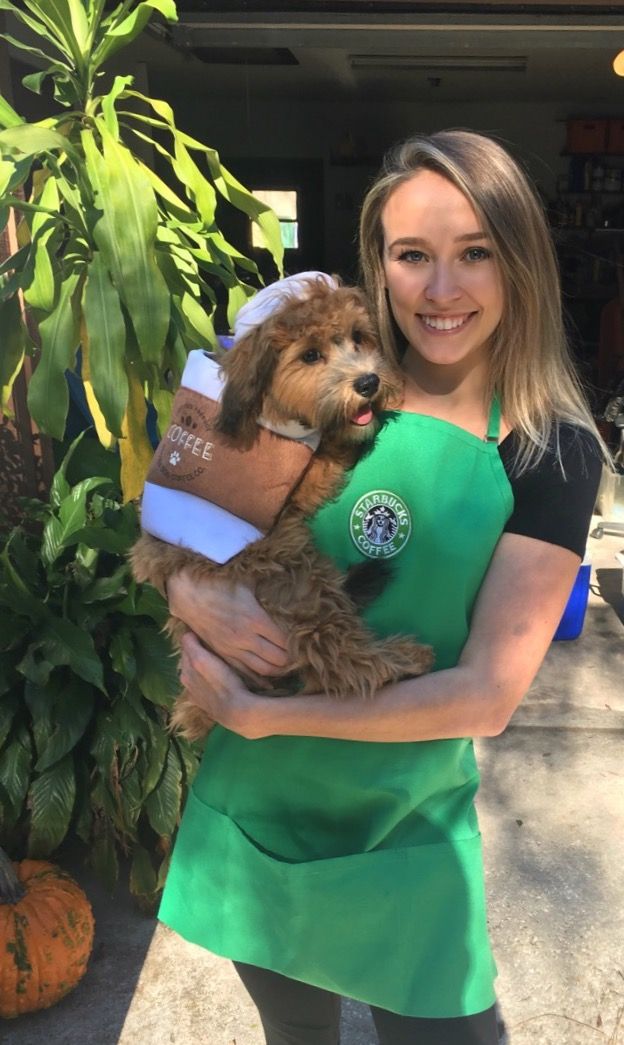 a woman is holding a dog wearing a starbucks apron and green hat while posing for the camera