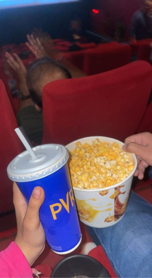 a person sitting in a red chair holding a blue cup with popcorn and a drink