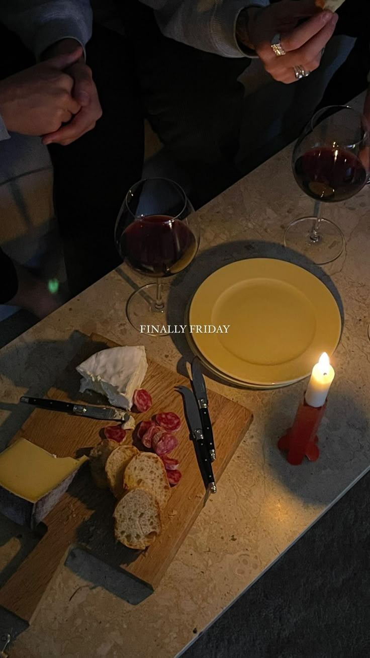 a table topped with cheese and bread next to glasses of wine on top of a wooden cutting board