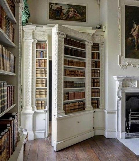 the room has many bookshelves in it, and there are paintings on the wall