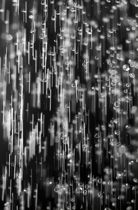 black and white photograph of rain drops falling from the sky in front of a dark background