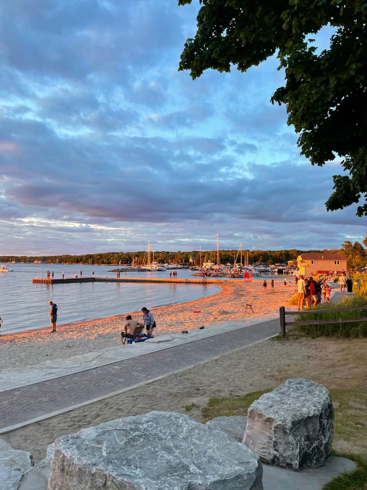 people are on the beach at sunset with boats in the water and rocks around them