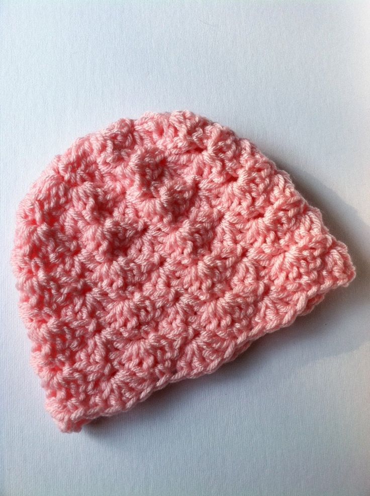 a pink crocheted hat sitting on top of a white table next to a pair of scissors