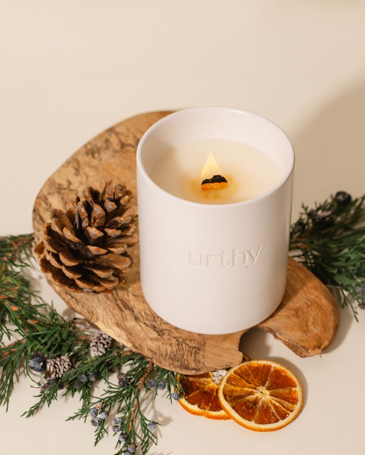 a white candle sitting on top of a wooden tray next to an orange and pine cone