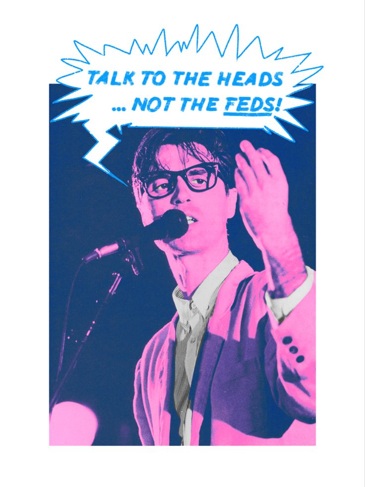 a man with glasses and a microphone in front of a sign that says talk to the heads not the feeds