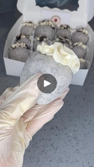 a person in white gloves is holding a box of chocolate truffles with frosting on top