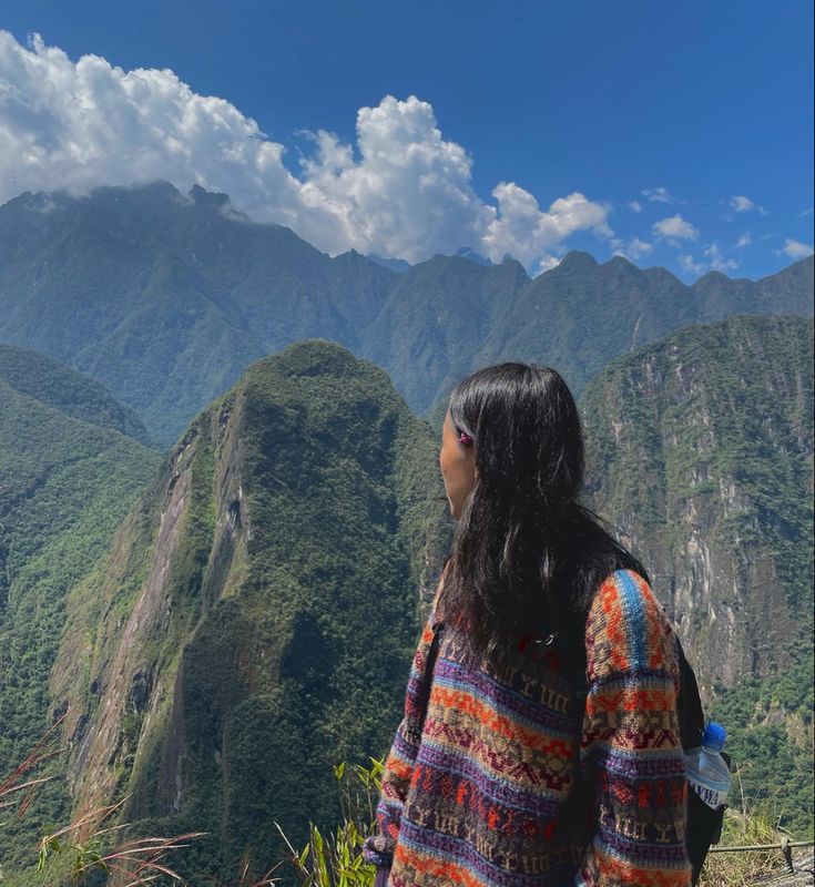 a woman standing on top of a mountain looking out at the mountains and clouds in the sky